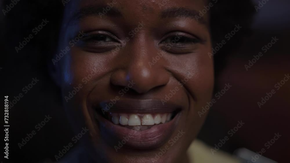 Close up of young black woman face smiling happy. African American female looking joyful to camera. Afro girl with positive attitude at night indoors. Natural beauty in millennial generation people