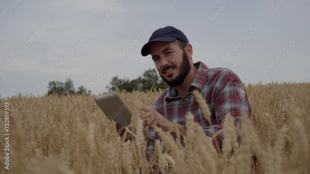 Smiling agronomist engineer using tablet to analyze state of wheat field sitting at ground looking camera. Technician worker man of agricultural industry. Crop control with modern digital technologies Smiling agronomist engineer using tablet to analyze state of wheat field sitting at ground looking camera. Technician worker man of agricultural industry. Crop control with modern digital technologies