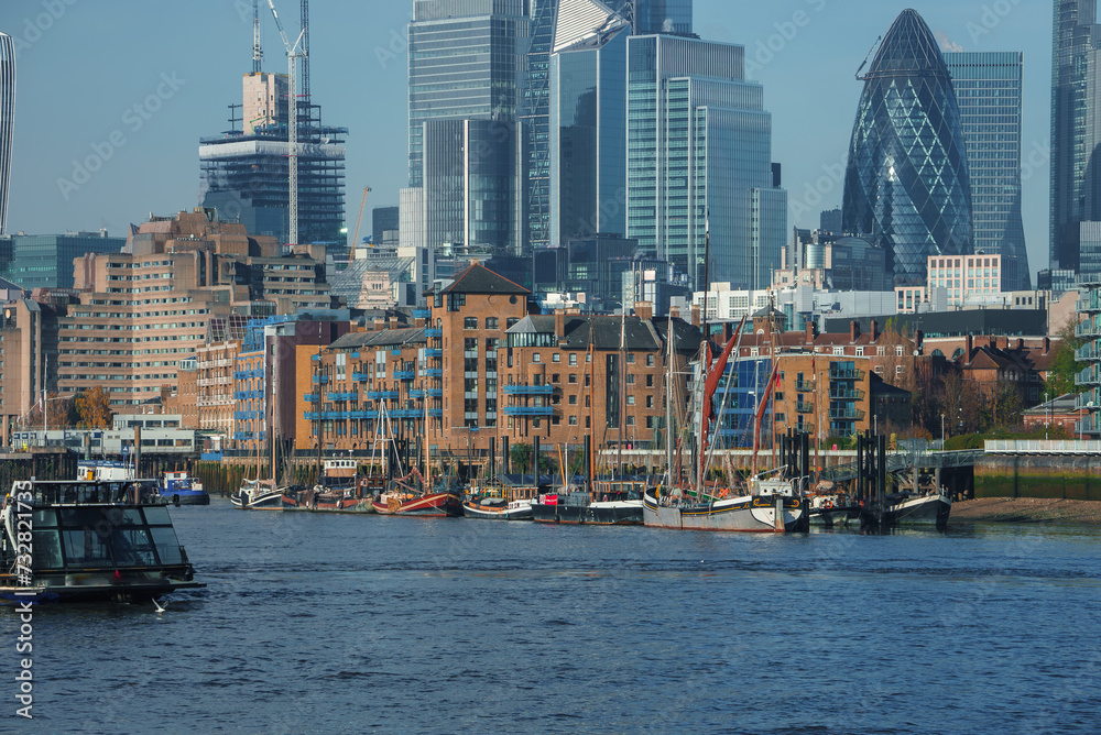 Fototapeta premium London's River Thames bustles with boats against a skyline featuring The Gherkin and a mix of historic and modern buildings, reflecting a clear day in the UK's capital.