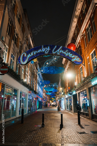 Festive London street scene with Carnaby Universe sign, colorful Christmas lights, and a mix of modern and traditional architecture, reflecting a vibrant holiday atmosphere. photo