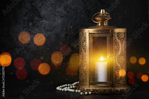 Muslim lantern with burning candle and prayer beads for Ramadan on dark background photo