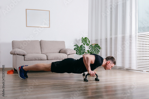 Athletic man performing calisthenics training session using a pushup bars. Bodybuilder doing bodyweight exercises at home.