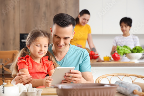 Little girl with her father using tablet computer in kitchen