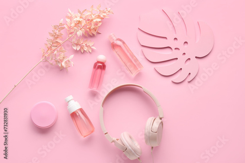 Composition with modern headphones, bottles of cosmetic products and leaf on pink background