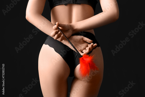 Young woman with feather stick on dark background, back view. Sex concept