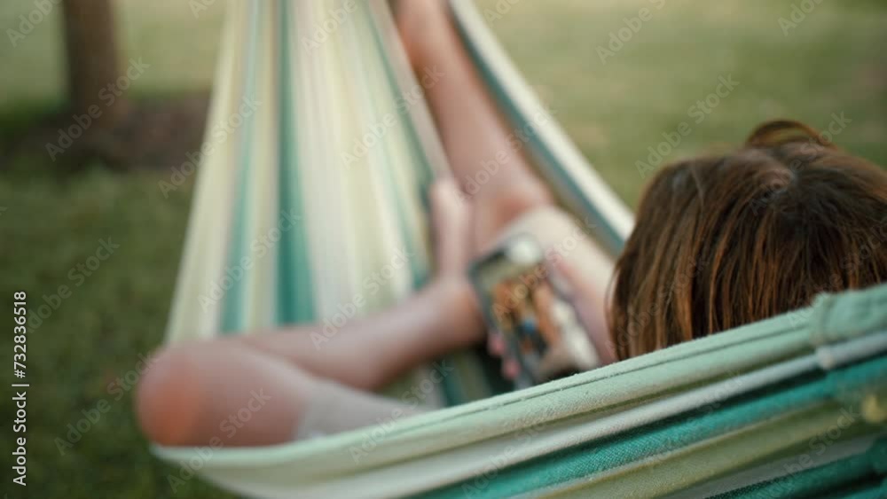 Child filmed from back chilling in garden hammock with his phone