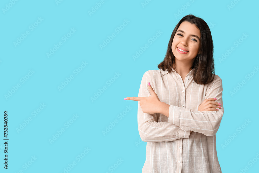 Young happy smiling woman pointing at something on blue background Young happy smiling woman pointing at something on blue background