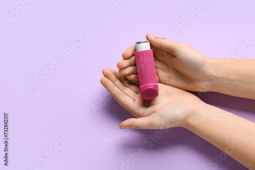 Child's hands with asthma inhaler on lilac background photo