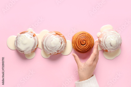 Female hand and tasty cinnamon rolls with glaze on pink background