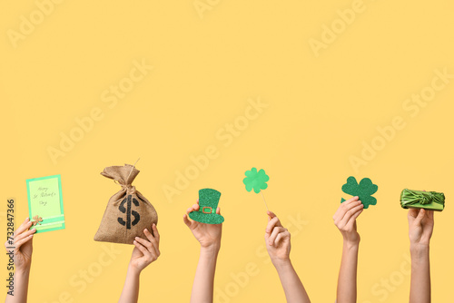 Female hands holding gift box and party decor for St. Patrick's Day celebration on yellow background
