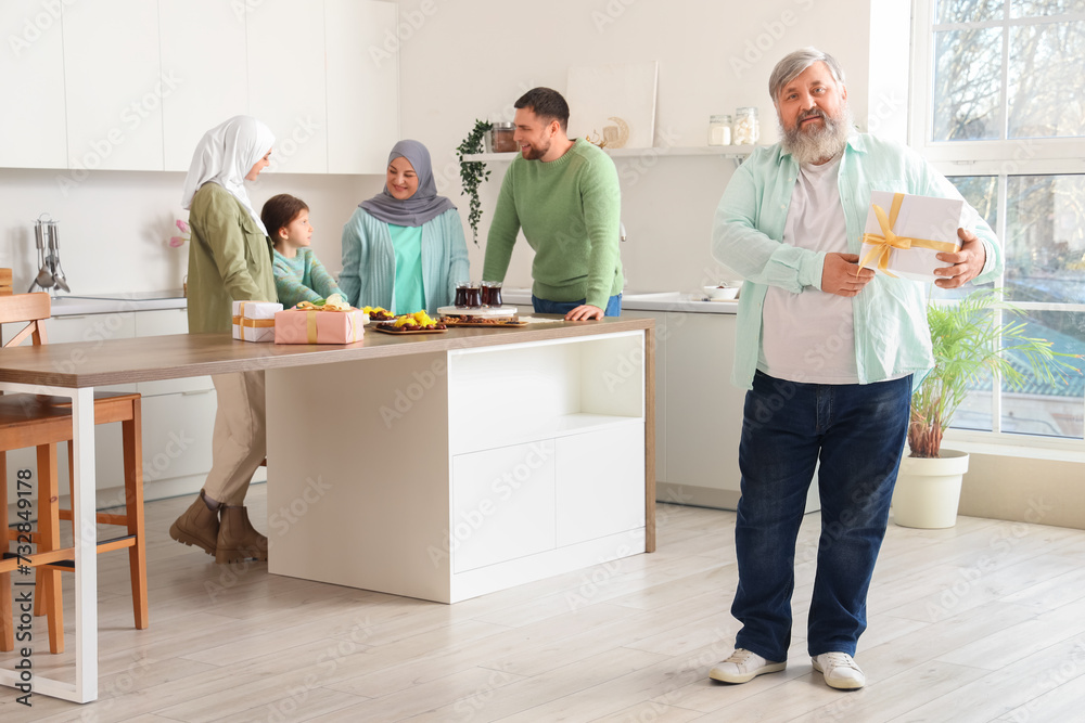 Mature Muslim man with gift and his family in kitchen. Ramadan celebration Mature Muslim man with gift and his family in kitchen. Ramadan celebration