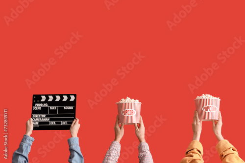 Many hands with buckets of popcorn and movie clapper on red background