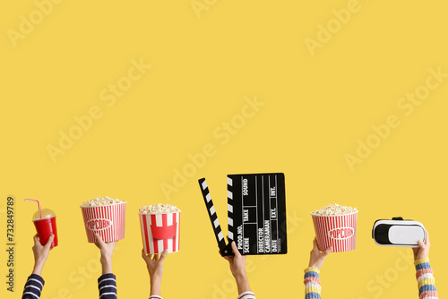 Many hands with buckets of popcorn, movie clapper and VR glasses on yellow background photo