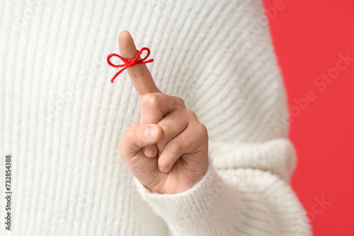 Woman with red bow on index finger against red background. Reminder concept photo