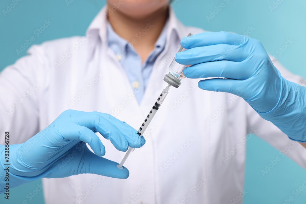 Doctor filling syringe with medication from glass vial on light blue background, closeup Doctor filling syringe with medication from glass vial on light blue background, closeup