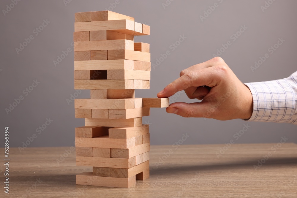 Playing Jenga. Man removing block from tower at wooden table against grey background, closeup Playing Jenga. Man removing block from tower at wooden table against grey background, closeup