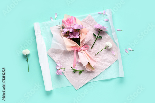 Composition with mini bouquet of beautiful spring flowers in wrapping paper on turquoise background. International Women's Day