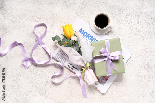 Mini bouquet of beautiful spring flowers in wrapping paper with newspaper, gift box and cup of coffee on white grunge background. International Women's Day