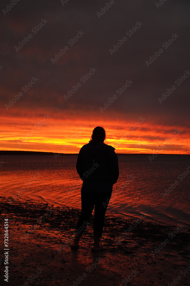 Woman standing on a beach watching an orange sunset