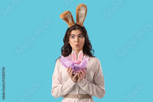 Surprised beautiful woman in bunny ears with Easter cake on blue background