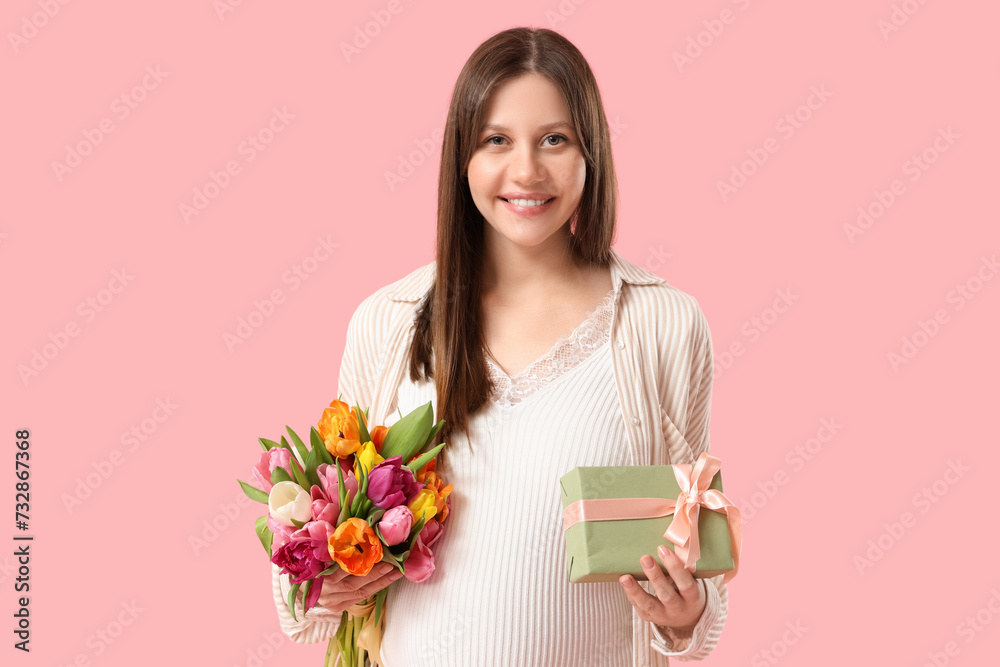 Beautiful young pregnant woman with bouquet of tulips and gift box on pink background. International Women's Day Beautiful young pregnant woman with bouquet of tulips and gift box on pink background. International Women's Day