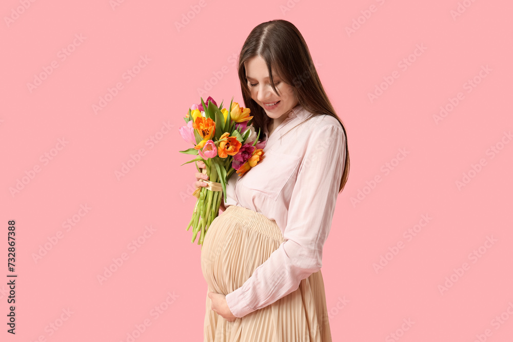 Beautiful young pregnant woman with bouquet of tulips on pink background. International Women's Day
