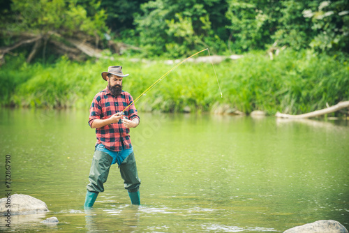 Young bearded man fishing at a lake or river. Flyfishing. Man pulling fishing rod.