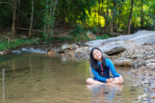nature water stream with asian child or kid girl sitting smiling playing in garden forest at phalad waterfall in lan sang national park at Tak Thailand for summer holiday relax and travel to happy fun