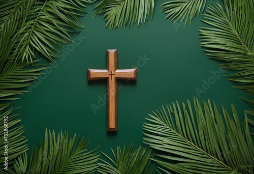 Wooden cross and palm leaves on dark green surface, from above