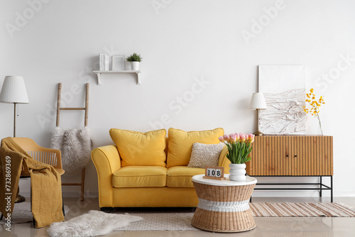 Interior of light living room with sofa and tulips in vase for International Women's Day