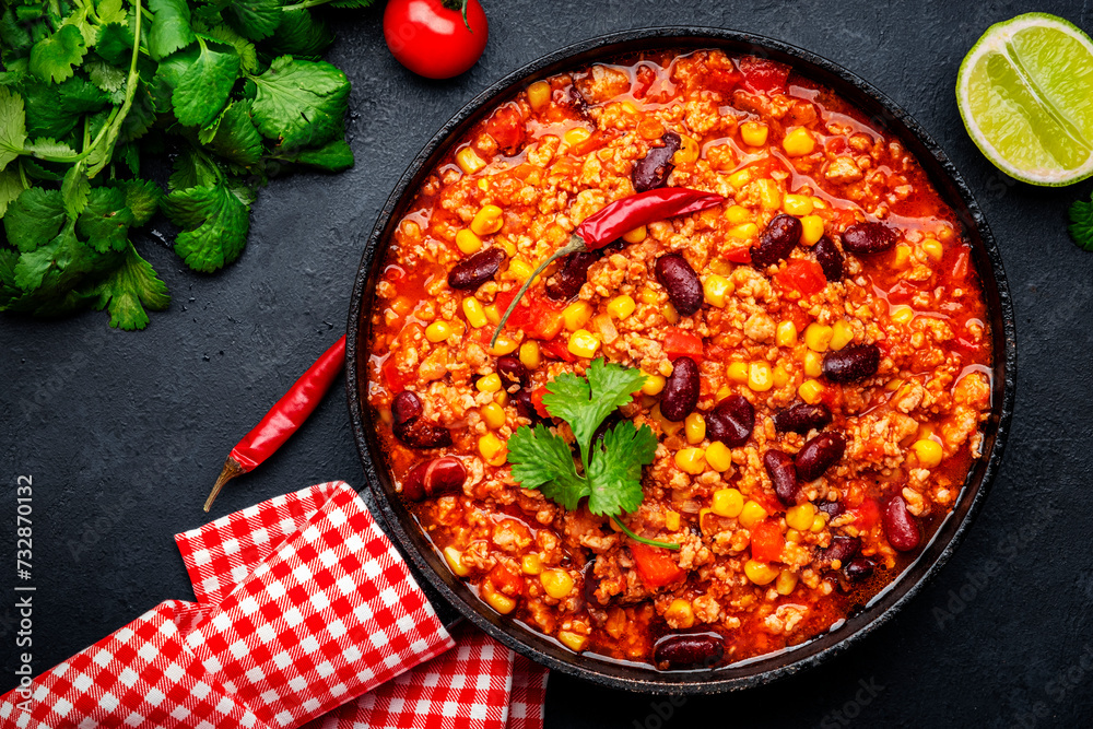 Chili con carne, mexican dish with minced beef, red beans, paprika, corn, cilantro and red peppers in spicy tomato sauce, tex-mex cuisine, black table background, top view