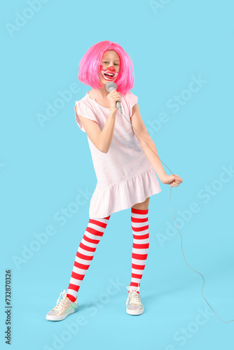 Funny girl in clown costume with microphone on blue background. April Fool's Day celebration