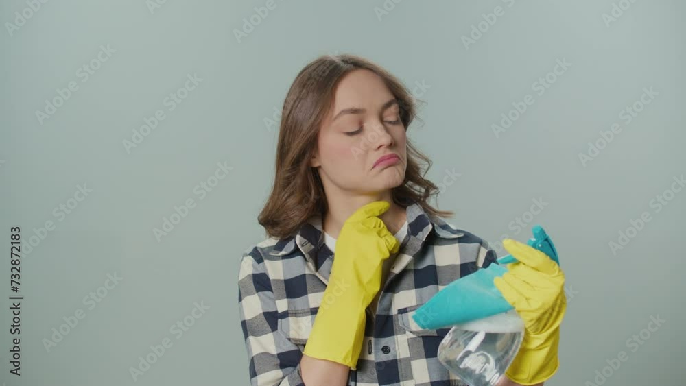 A Portrait of a Thoughtful Young Woman in Yellow Gloves,Holding a Cleaning Spray Bottle and Rag on the Gray Background.A Female Housewife Thinks Where to Start Cleaning. Hygiene and Safety Protocols. A Portrait of a Thoughtful Young Woman in Yellow Gloves,Holding a Cleaning Spray Bottle and Rag on the Gray Background.A Female Housewife Thinks Where to Start Cleaning. Hygiene and Safety Protocols.