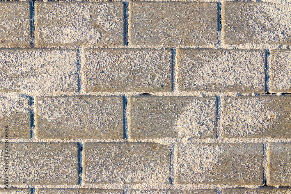 Obraz premium Horizontal texture of paving slabs made of artificial stone or concrete is laid and seams are covered with sand, the remains of which are on the surface, selective focus