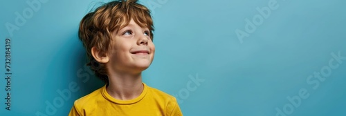 Boy in yellow shirt looking up on a blue background.