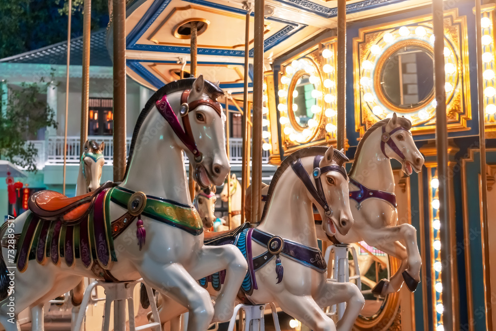 Old French carousel spins in a holiday park. Elephant horses on a traditional vintage fairground carousel, evening at night with bright lights and flashes.