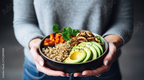 Healthy vegetarian dinner. Woman in jeans and warm sweater holding bowl with fresh salad, avocado, grains, beans, roasted vegetables, close-up. Superfood, clean eating.