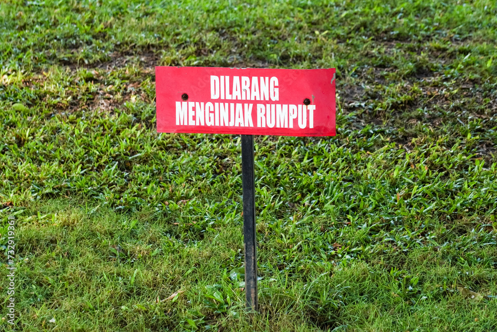 A red board that says no stepping on grass is placed in a public park.