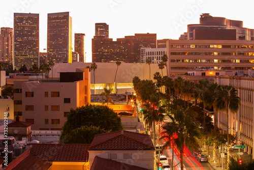 Twilight view of traffic streaming down Rodeo Drive with historic downtown skyline of Beverly Hills, California, USA.