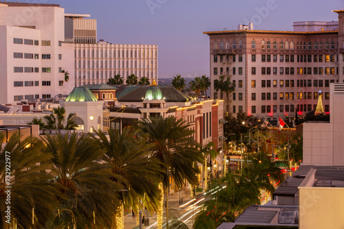 Twilight view of traffic streaming down Rodeo Drive with historic downtown skyline of Beverly Hills, California, USA.
