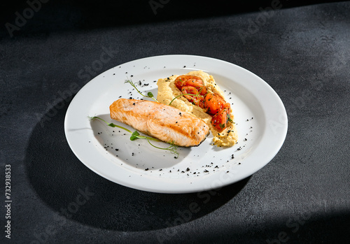 Salmon steak with hummus and tomatoes on a white plate
