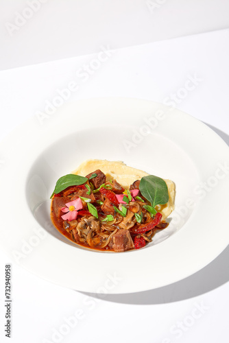 Braised beef with vegetables and mushrooms served with mashed potatoes, on an isolated white background, a hearty meal