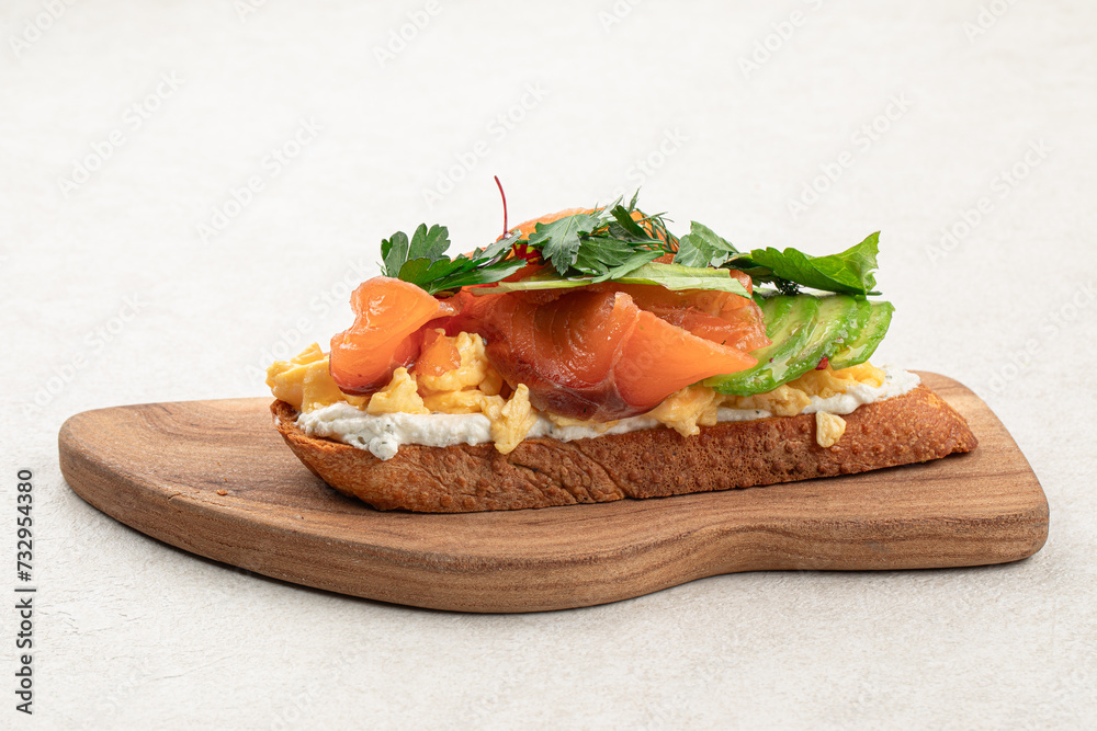 Breakfast toast with salmon and avocado on wooden board