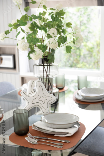 White and brown plate setting on dinning table with flowers vase in a dining room photo