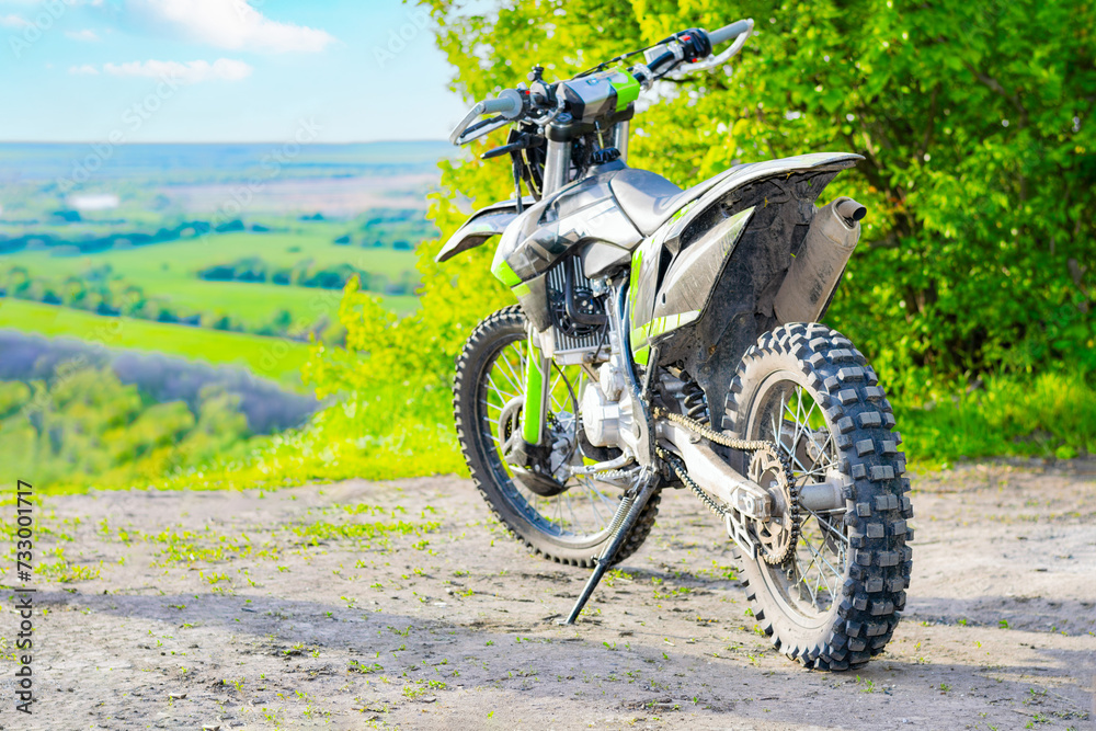 an extreme cross enduro motorcycle stands on a hill overlooking a field and a blue sky with clouds. concept of traveling through nature on a motorcycle. close-up an extreme cross enduro motorcycle stands on a hill overlooking a field and a blue sky with clouds. concept of traveling through nature on a motorcycle. close-up