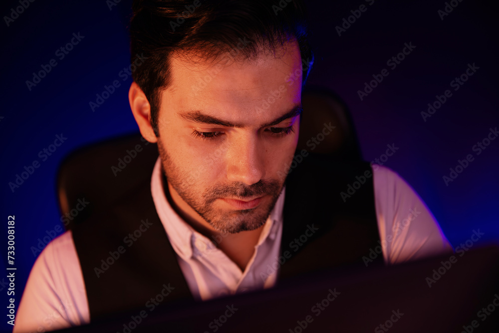 Portrait feeling bored businessman waiting analyzing market data or e-mail sending back to customer preparing created on sales channel online product at neon dark light at late night time. Surmise.