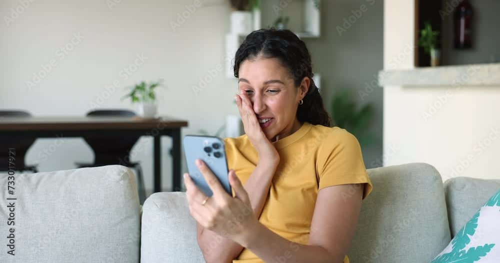 Overjoyed Latina girl sit on sofa in living room, hold smartphone, get message, feel happy with good surprising news, laugh, celebrate online lottery victory. Moment of win, jackpot, new app or game Overjoyed Latina girl sit on sofa in living room, hold smartphone, get message, feel happy with good surprising news, laugh, celebrate online lottery victory. Moment of win, jackpot, new app or game