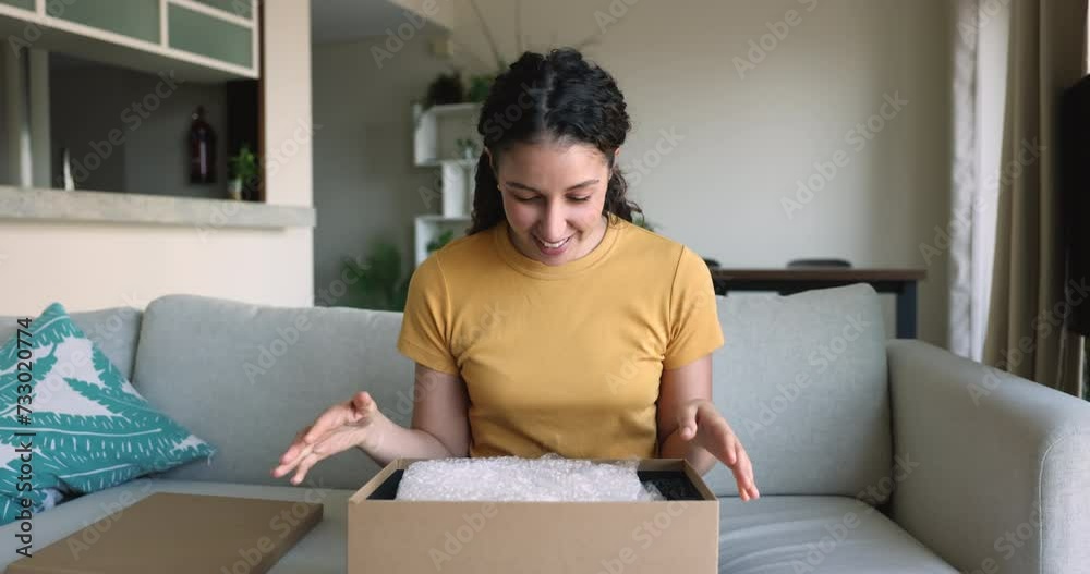 Happy Brazilian woman sit on sofa opening parcel box enjoy received gift from friend, get goods bought through marketplace website. Express delivery services, client of electronic commerce, e-shopping Happy Brazilian woman sit on sofa opening parcel box enjoy received gift from friend, get goods bought through marketplace website. Express delivery services, client of electronic commerce, e-shopping