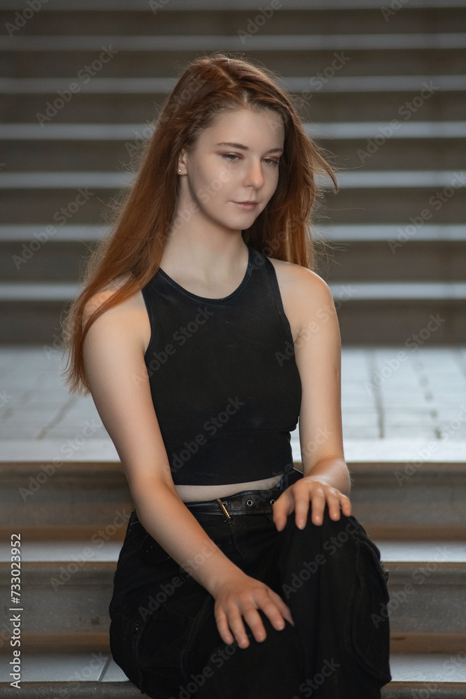 Portrait of a young beautiful long-haired girl in dark clothes on a summer street.