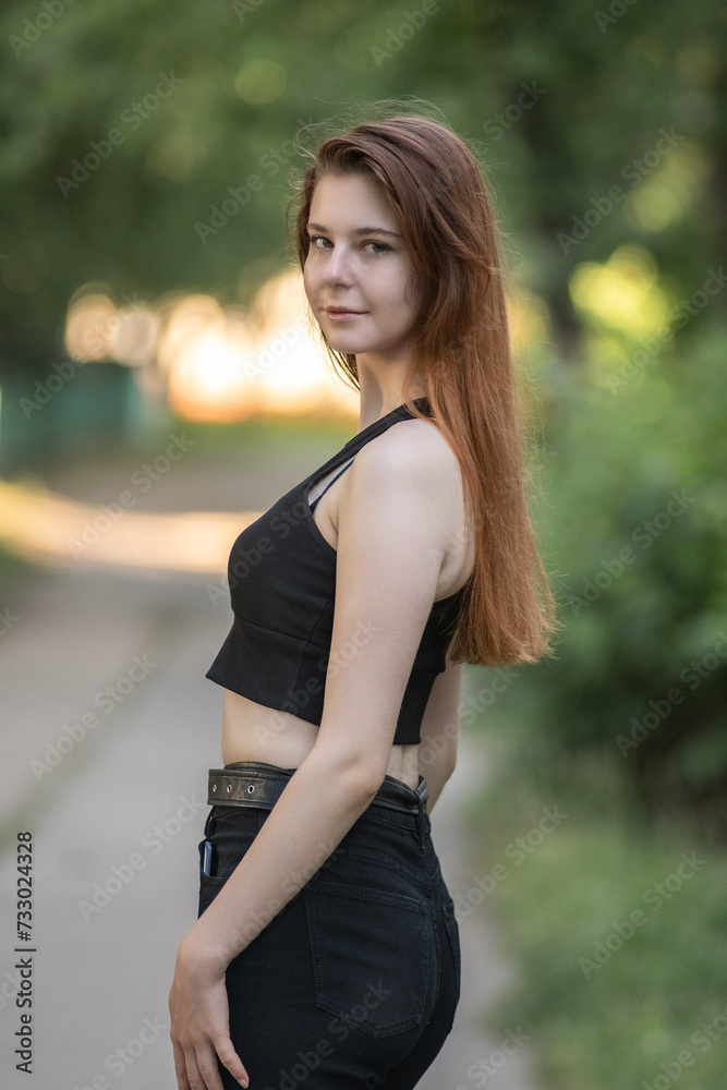 Portrait of a young beautiful long-haired girl in dark clothes on a summer street.